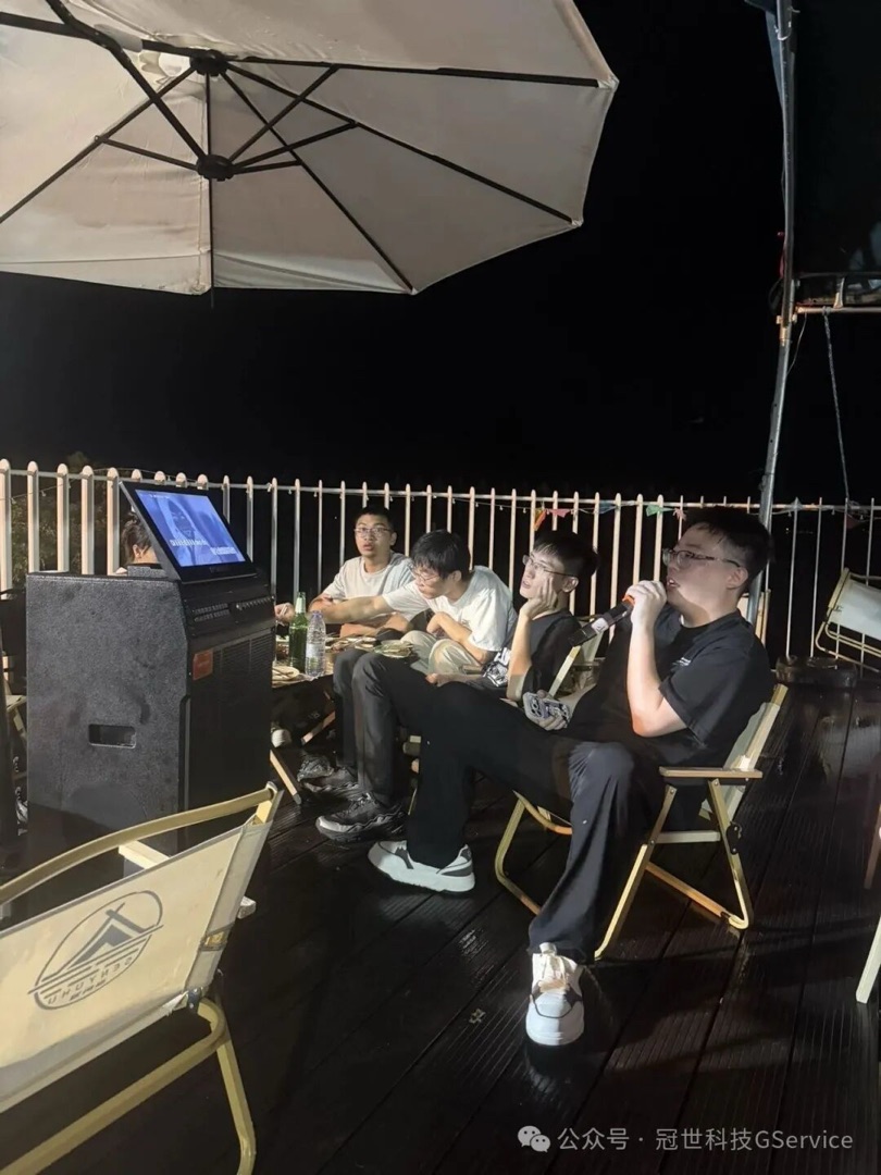 夜晚露营烧烤区，冠世科技同事围坐在一起唱歌聊天，桌上摆着烧烤